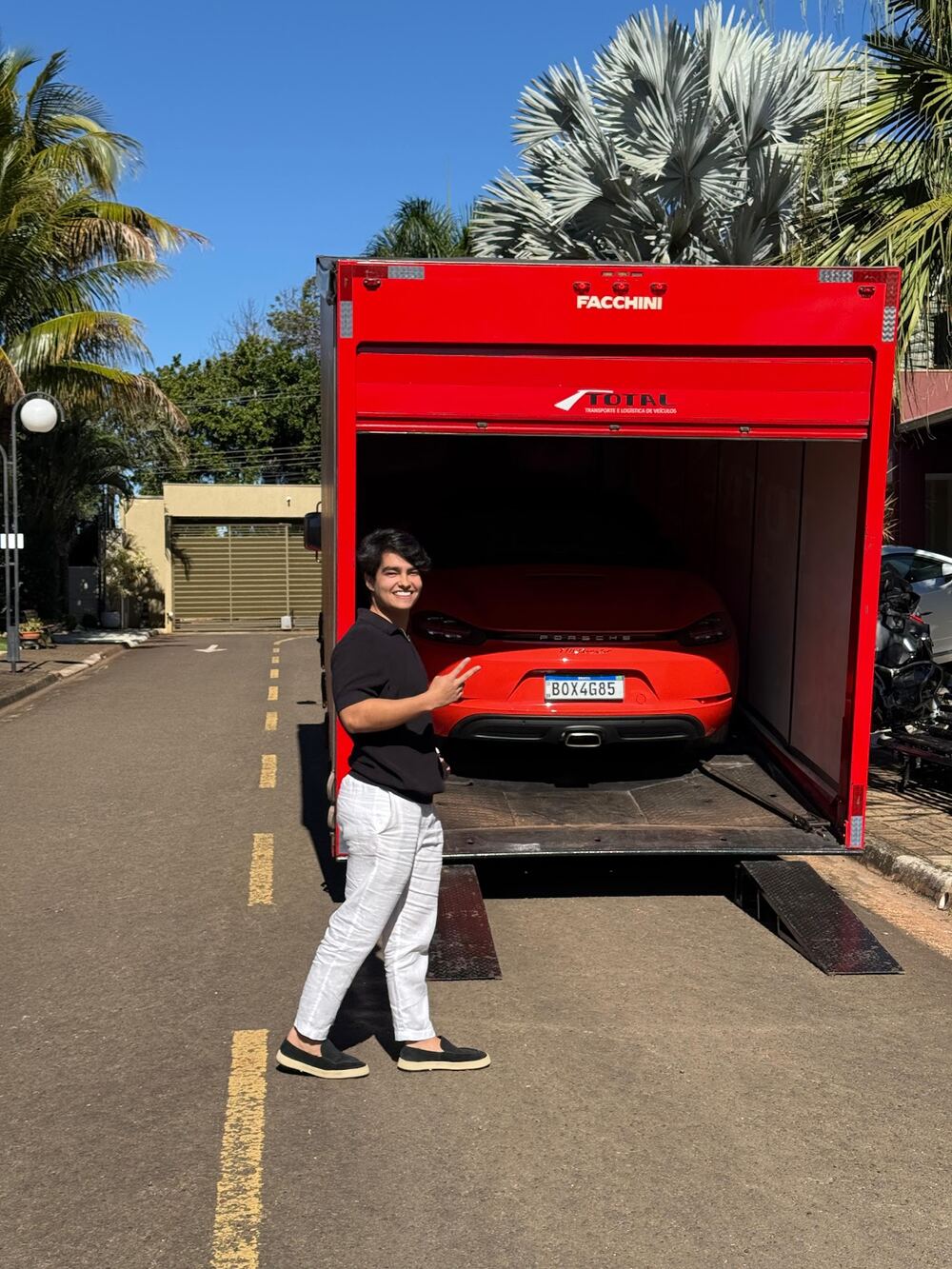 Murilo Bono ao lado do seu Porsche sendo entregue por caminhão-cegonha